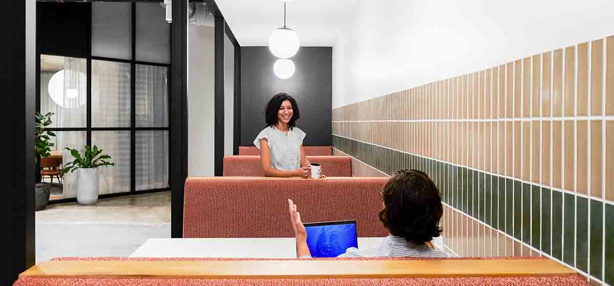 Photo of people talking across seating booths in an office (Tier 1_Office_Houston_AML_3535)